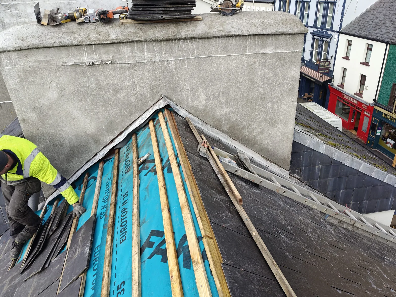 A slate roof being repaired around a chimney with new battens